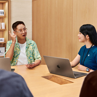MacBook'u olan bir Apple Store çalışanı, bir kişiyle etkileşime giriyor.