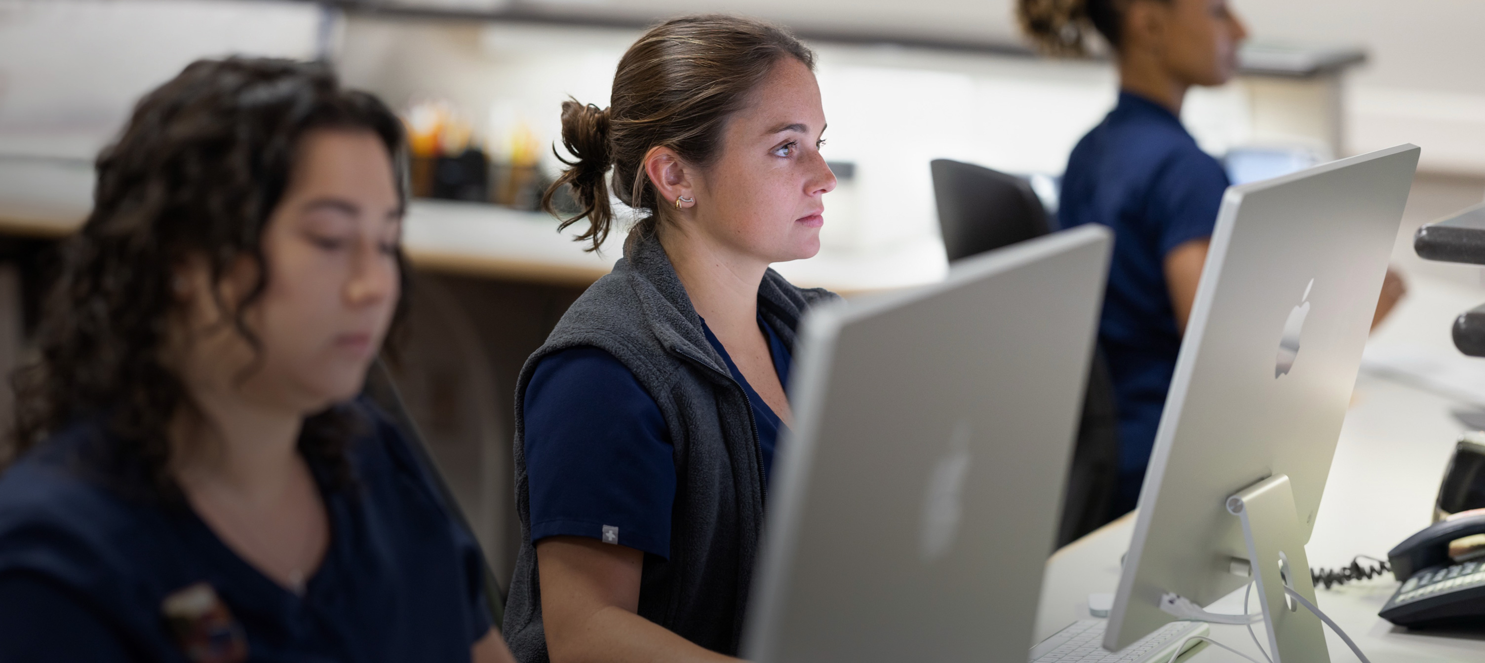 Drei Krankenschwestern arbeiten hinter iMac Displays.