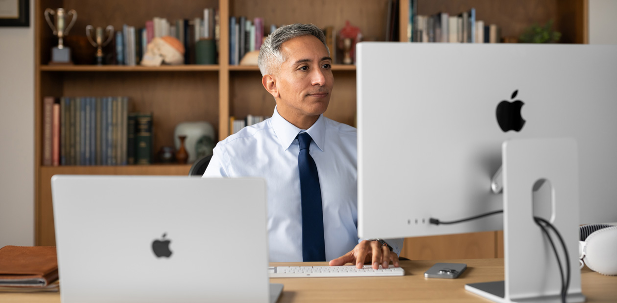 A provider sitting at his desk while looking at an iMac and MacBookPro.