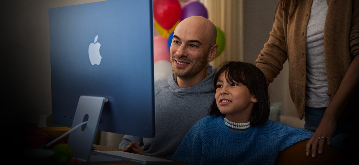 Hai người ngồi cùng nhau sử dụng iMac trong khi một người thứ ba đứng phía sau quan sát.